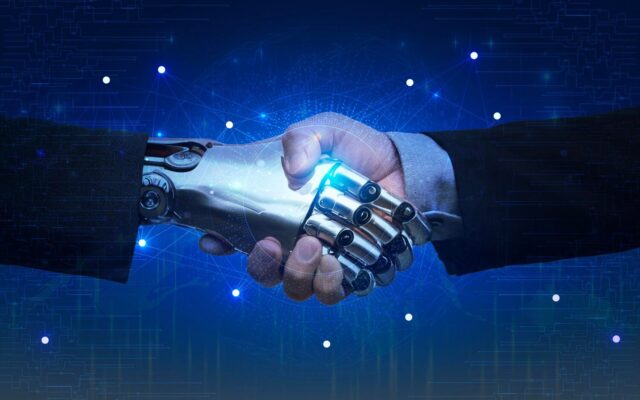 Emberi és robotkéz fog kezet, ami az ember és a mesterséges intelligencia együttműködését szimbolizálja kék digitális háttér előtt.