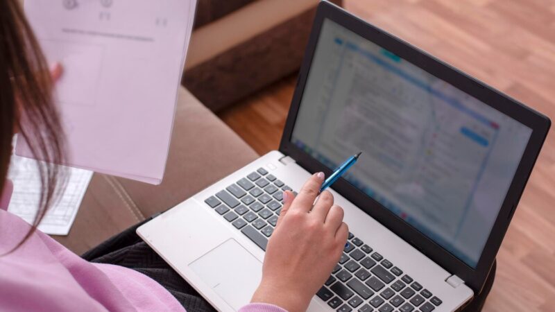 Nő tollal a kezében ellenőriz egy szöveget a laptopja képernyőjén