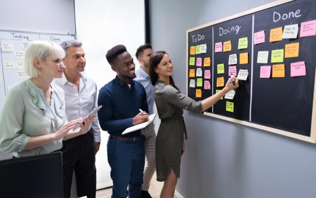 Kollégák egy kanban-táblán rendezik a feladatokat öntapadós cetlikkel