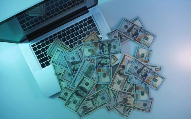 Nyitott laptop billentyűzetén és mellette szétszórt százdolláros bankjegyek felülnézetből.