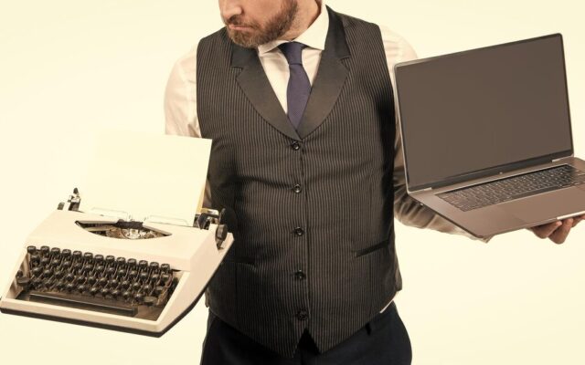 Férfi az egyik kezében mechanikus írógépet, a másikban modern hordozható laptopot tart.